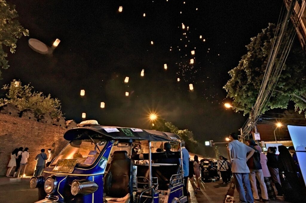 tuk-tuk en premier plan avec des lanternes lâchées dans les airs pour la fête des lumières