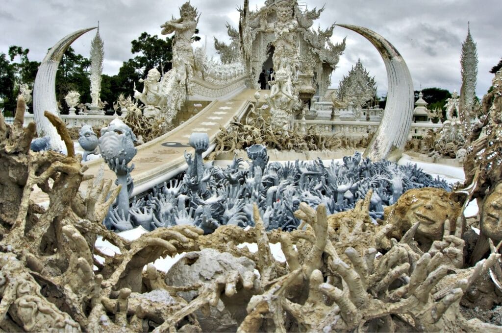 sculptures de mains blanches sortant du sol devant le temple blanc à Chiang Rai