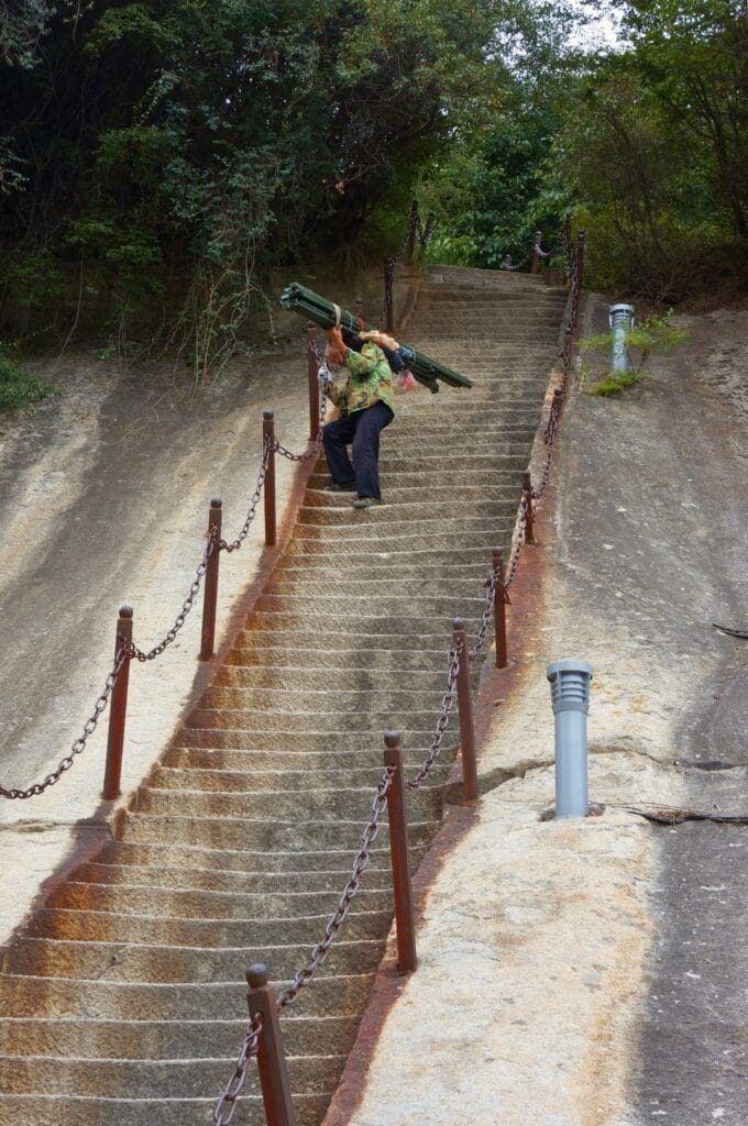 Chinois portant un lourd chargement en train de descendre un escalier escarpé et taillé dans la roche