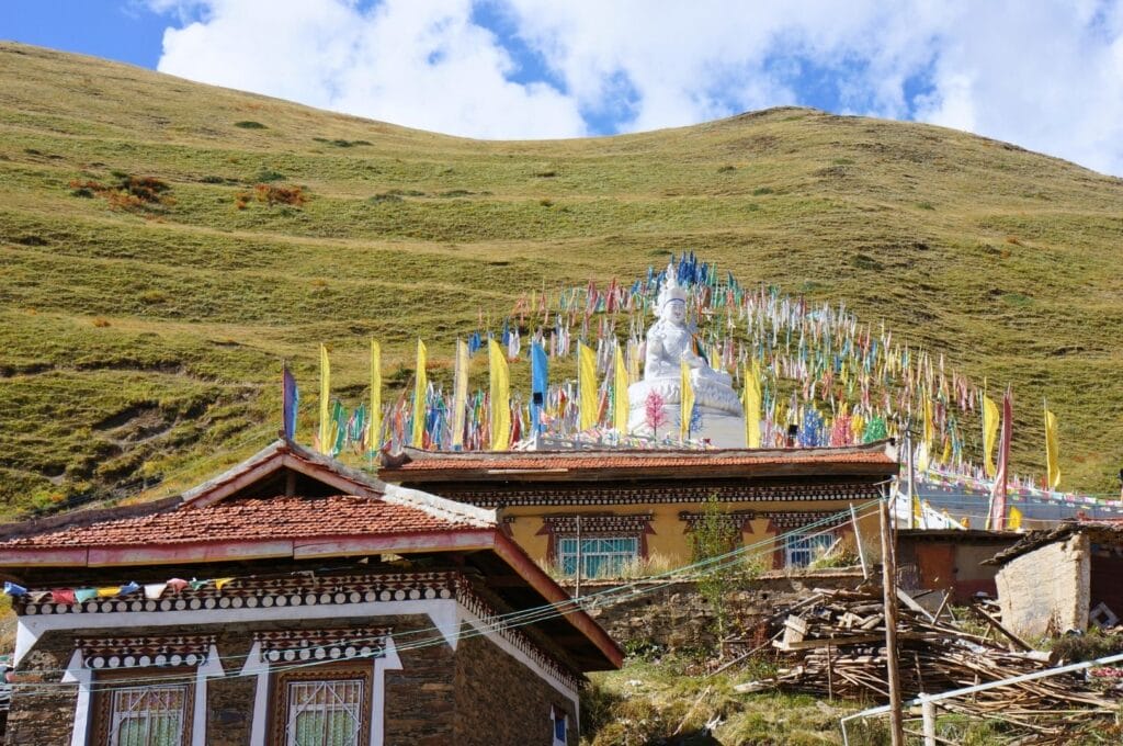 statue de bouddha blanche entouré de drapeaux colorés sur les flancs d'une montagne